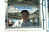 [Photo: Captain at the wheel in pilothouse ]