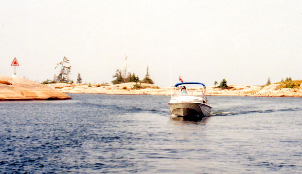 [Photo: Chris at helm, low rocky shore]