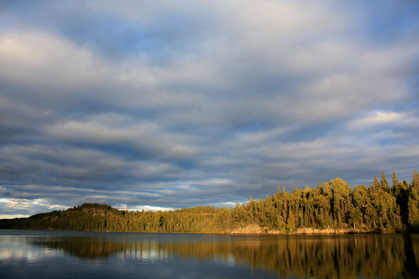 Photo: Low sun illuminates the shoreline with a cloudy sky in background.