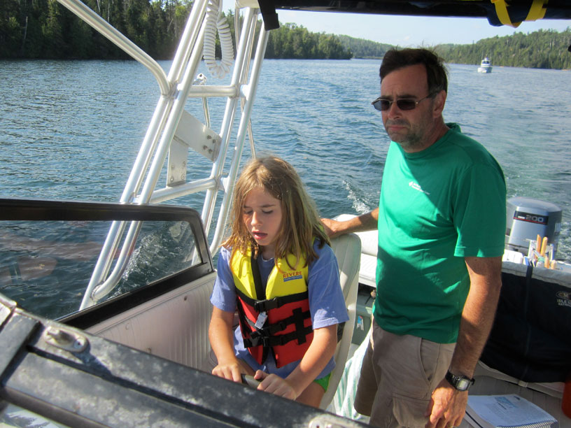 Photo: Young girl at helm with father watching.